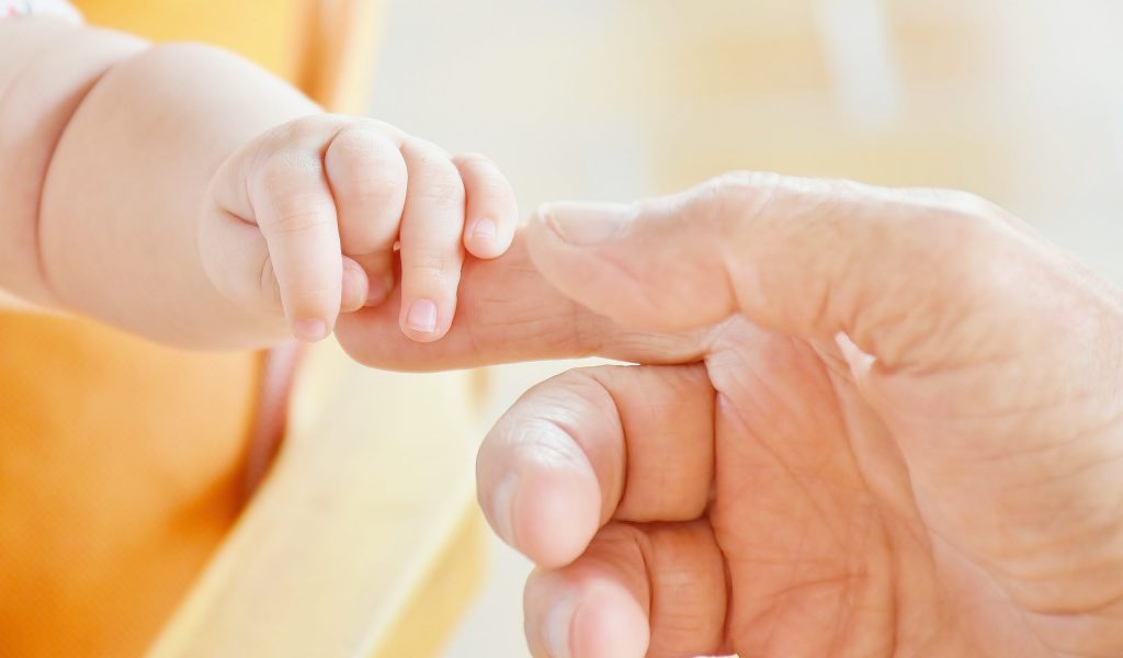 A close up image of an infant holding an adults finger